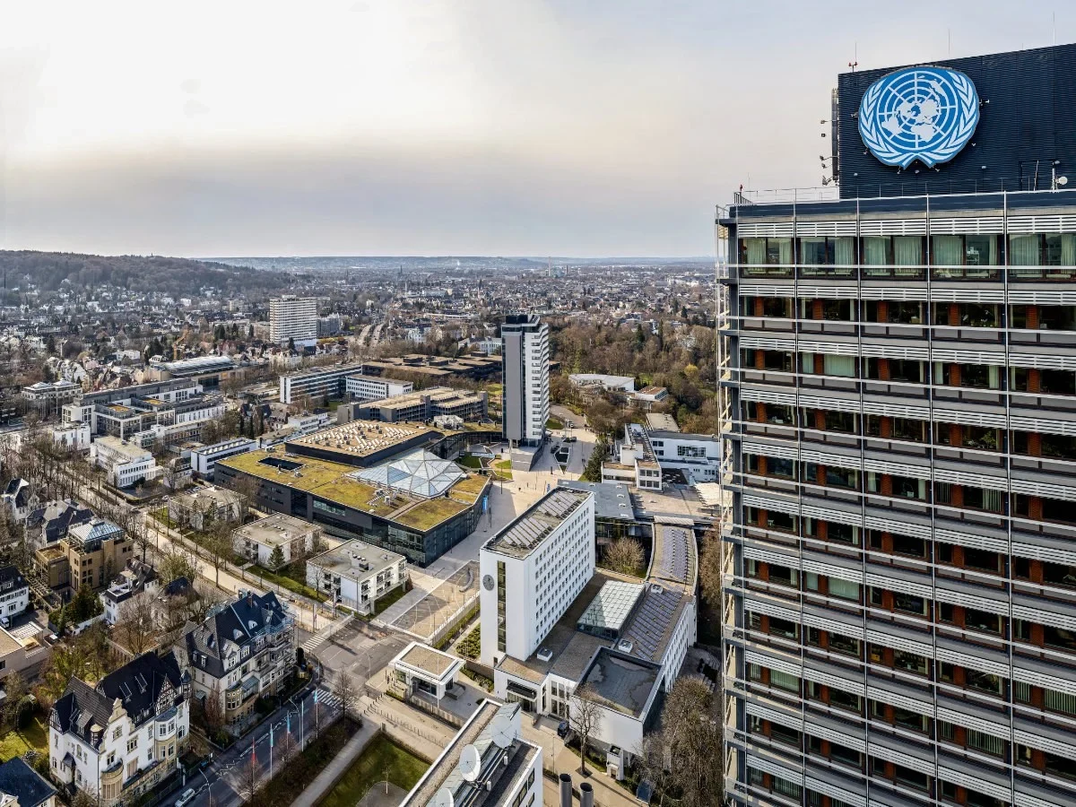Eine Wissenschaftlerin und ein Wissenschaftler arbeiten hinter einer Glasfassade und mischen Chemikalien mit Großgeräten.